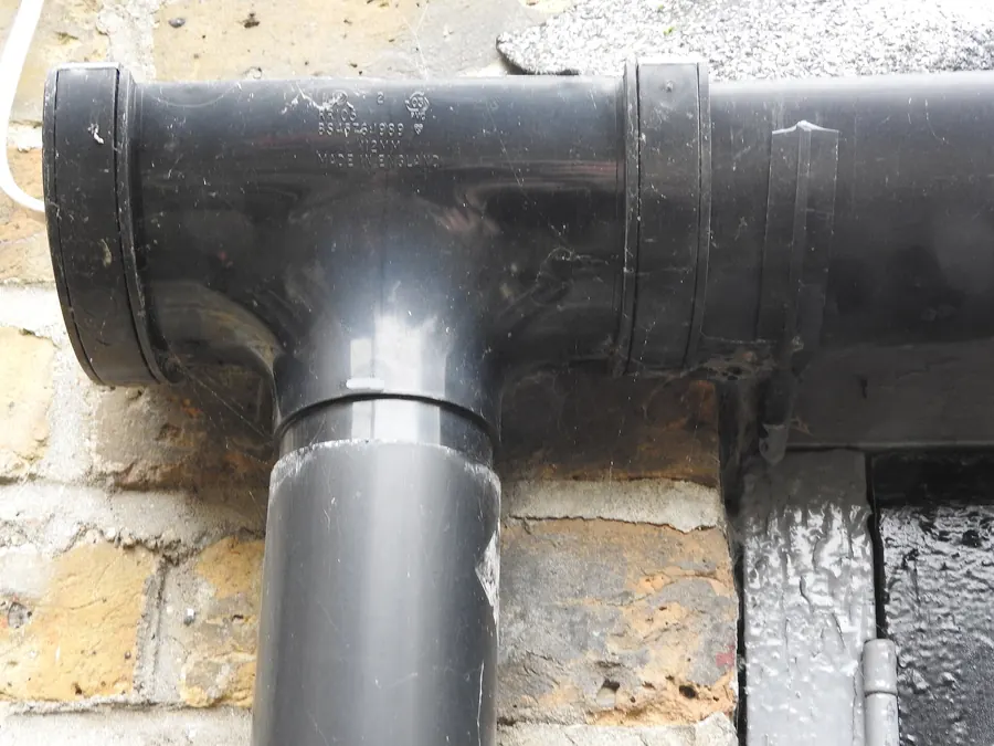 Black uPVC gutter running outlet and downpipe fixed against yellow stock brickwork