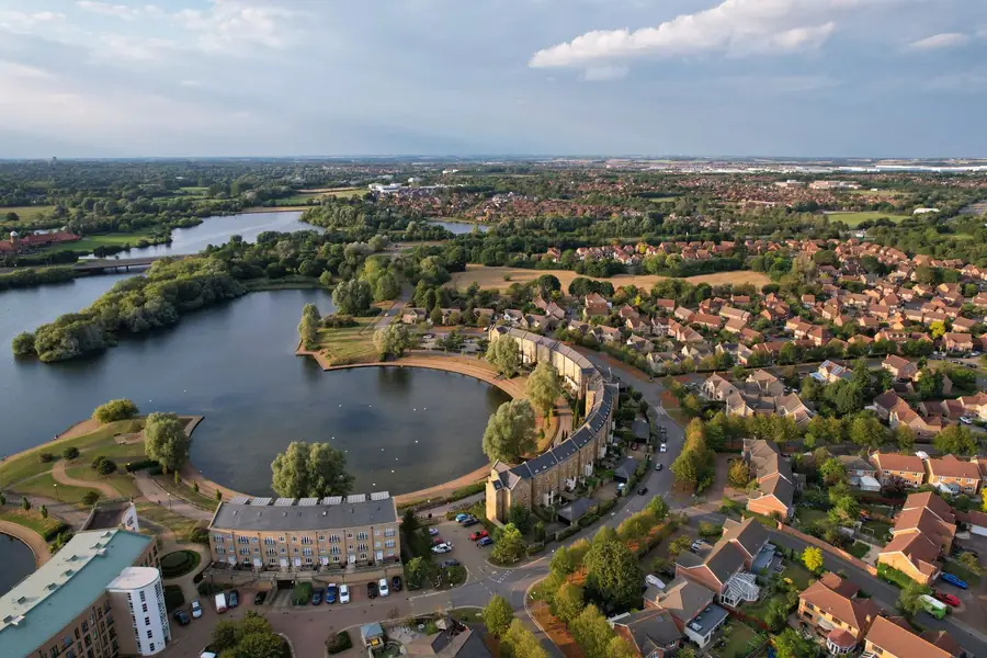 Aerial view of a modern English housing estate with brown and red tiled roofs beside a lake