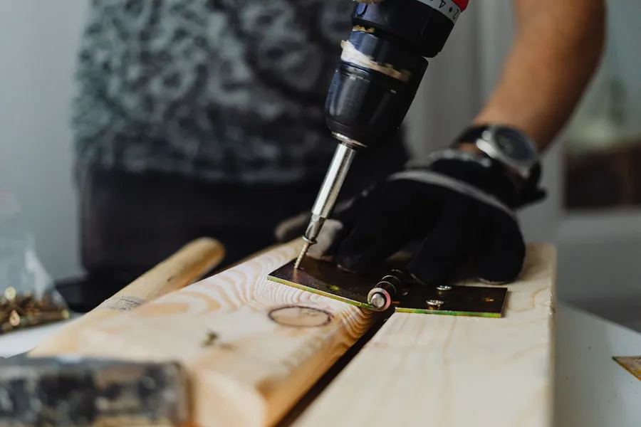 Gloved hand driving a screw into a length of new timber with a cordless drill