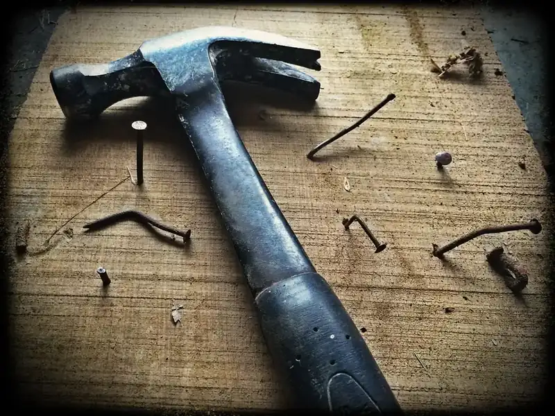 Claw hammer and bent nails on a worn timber board, a reminder of the small materials cost behind an emergency roof repair