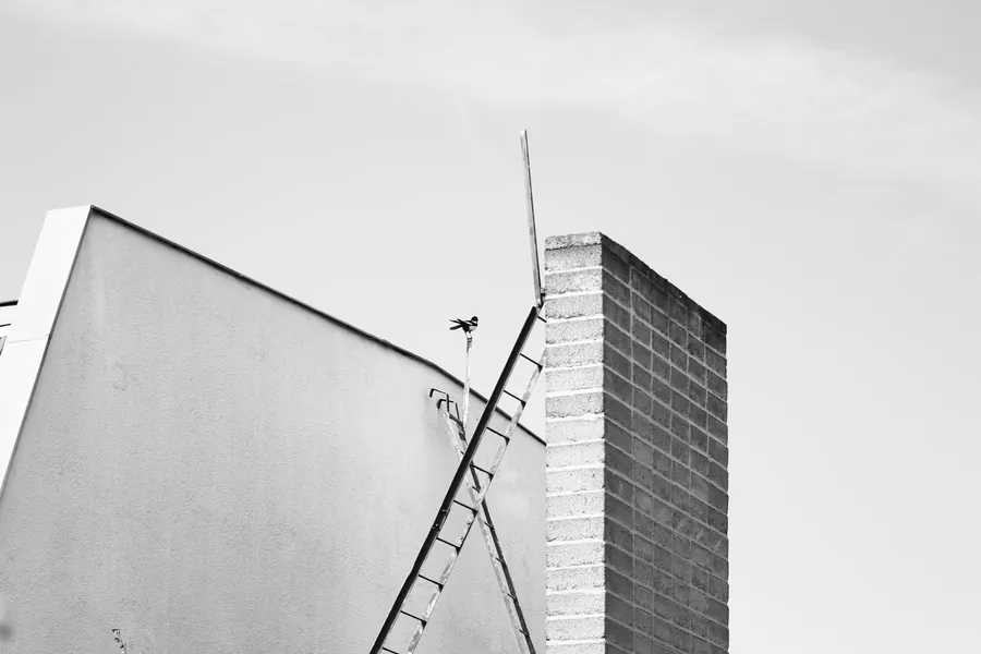 Ladder propped against a gable wall beside a brick chimney stack, ladder access for a small roof repair in Dartford