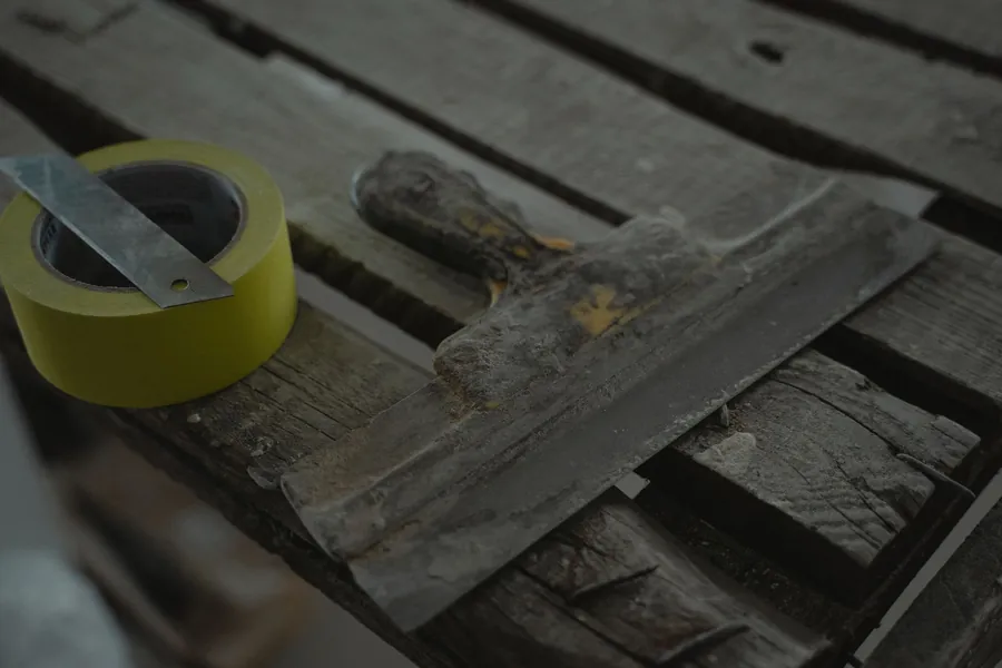 Scraper and a roll of tape resting on weathered timber boards, the makings of a quick patch repair