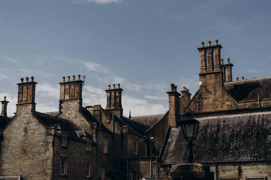 Tall stone chimney stacks with clusters of pots rising above the slate roofs of an old building