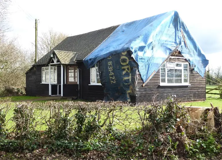 Blue tarpaulin roped over a damaged pitched roof as a temporary weatherproof cover
