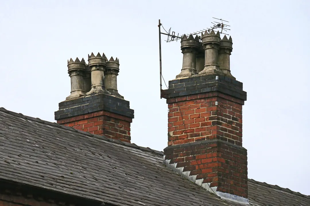 Two red brick chimney stacks with crowned clay pots and stepped lead flashing rising from a slate roof