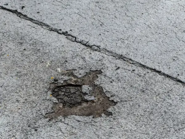 Close-up of a worn bitumen felt flat roof with a split seam and a patch where the top layer has broken away