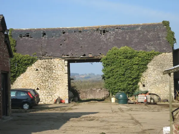 Old slate roof on a stone building with many slates missing or slipped, leaving open holes along the roof