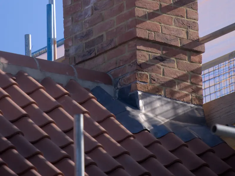 New grey lead flashing dressed round the base of a freshly pointed brick chimney on a clay tile roof