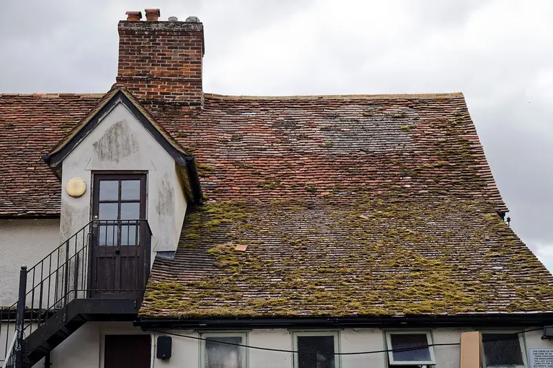 Old clay tiled roof with heavy moss and lichen, a dormer and a brick chimney stack