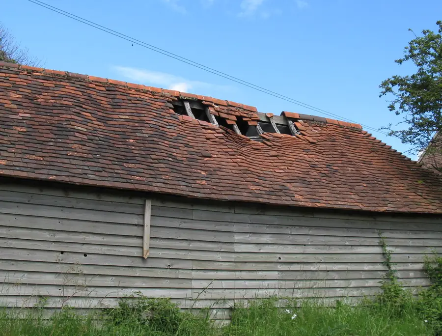 Old peg-tiled roof with a run of tiles missing near the ridge, exposing the battens underneath