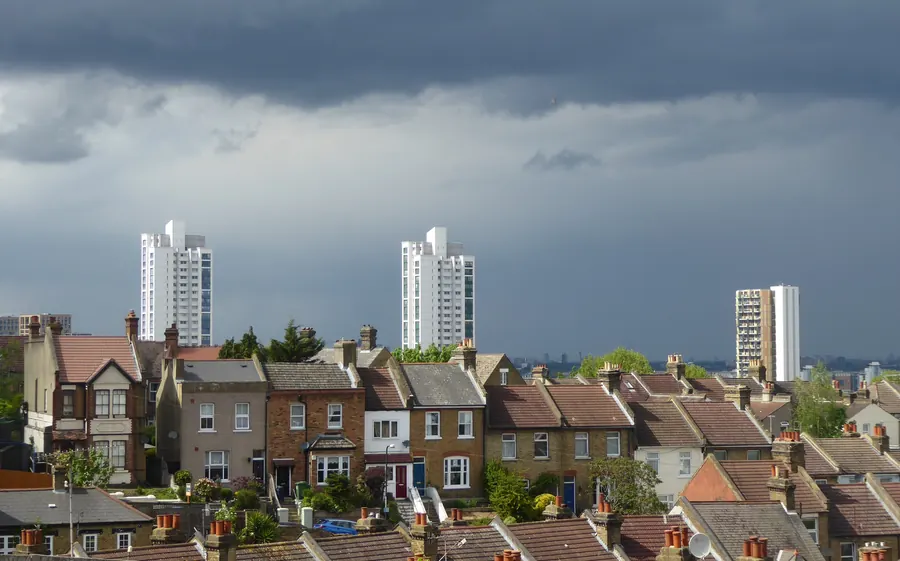 Dark storm clouds building over rows of terraced house roofs and chimneys in Plumstead, south-east London