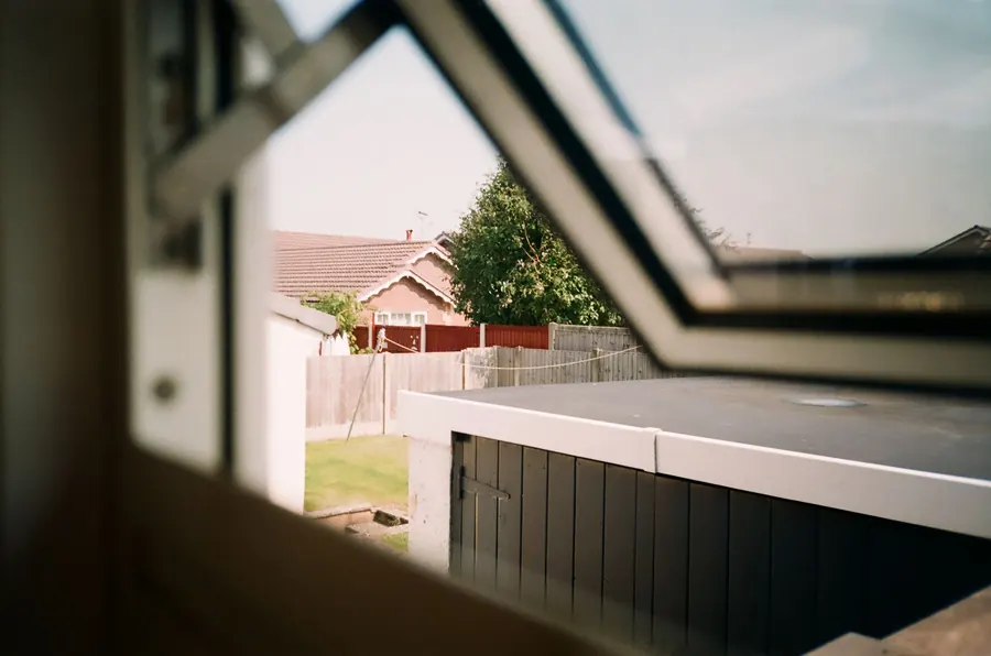 View out through an open roof window over back gardens, a flat-roofed outbuilding and a tiled bungalow roof